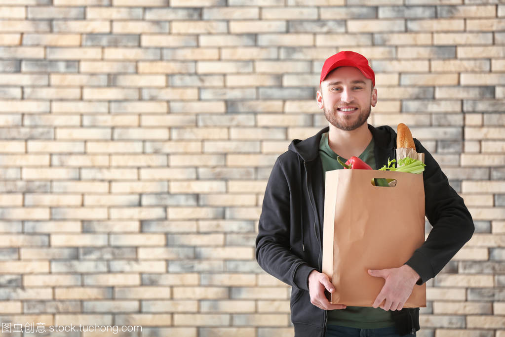 年轻人与产品在纸袋子在砖墙背景。食品配送服务